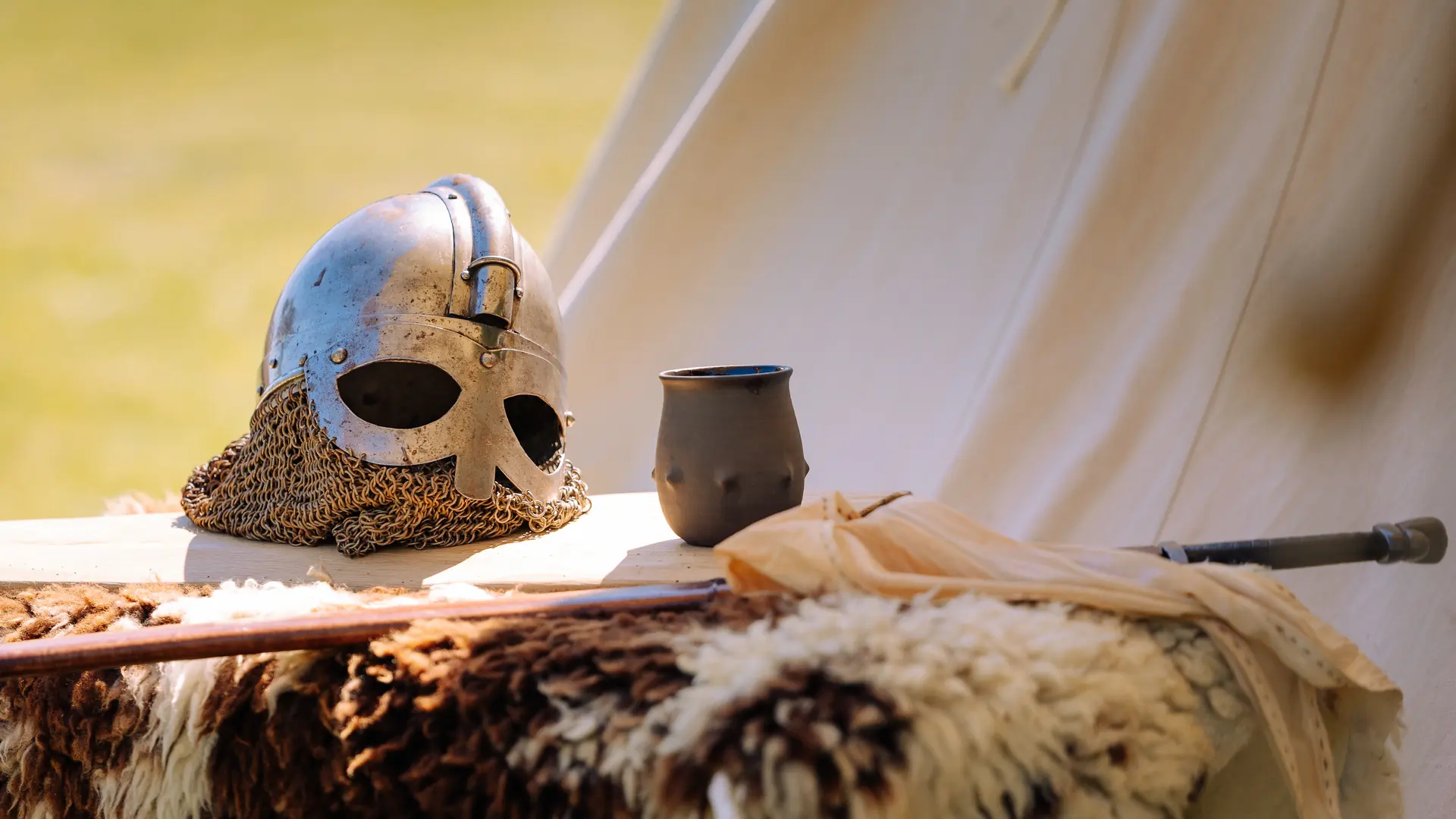 Wikingerhelm mit Kettenhaube und Trinkbecher auf einem Fell vor einem Zelt